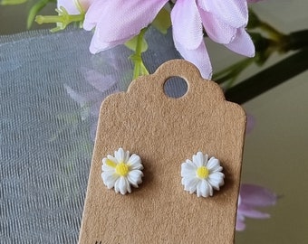 May include: A pair of white daisy earrings with yellow centers on a brown card with the text "Hand Made With Love Thank You" and a red heart.