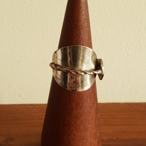 May include: A silver ring with a twisted wire design and a hammered metal band. The ring is displayed on a wooden ring holder.