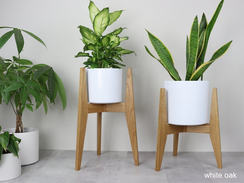 May include: Two white plant pots on wooden stands. The stands are made of white oak wood and have a simple, modern design. The pots are both white and cylindrical.