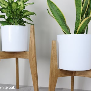 May include: Two white ceramic plant pots on wooden stands. The stands are made of white oak and have a simple, modern design. The pots are empty and ready to be filled with plants.