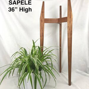May include: A wooden plant stand made of sapele wood. The stand is 36 inches tall and has a rectangular top. The stand is shown with a green plant in a white pot.