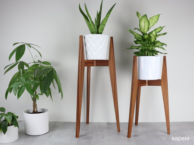 May include: Two wooden plant stands with white ceramic pots and green plants. The stands are made of dark wood and have a simple, modern design. The stands are about 30 inches tall.