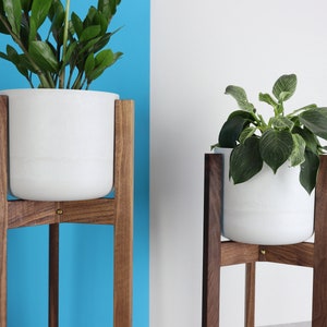 Puede incluir: Dos macetas blancas sobre soportes de madera. Los soportes son de madera de nogal y tienen un dise&ntilde;o simple y moderno. Las macetas son redondas y tienen un acabado blanco liso.