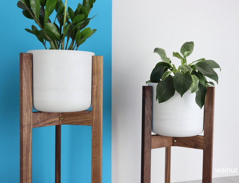 Puede incluir: Dos macetas blancas sobre soportes de madera. Los soportes son de madera de nogal y tienen un dise&ntilde;o simple y moderno. Las macetas son redondas y tienen un acabado blanco liso.