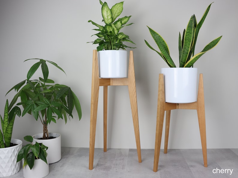 May include: Two wooden plant stands with white ceramic pots and green plants. The stands have four legs and are made of natural wood.