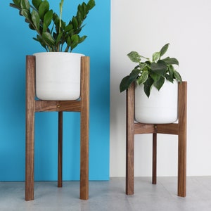 Puede incluir: Dos macetas de cer&aacute;mica blanca sobre soportes de madera. Los soportes son de madera de nogal y tienen un dise&ntilde;o simple y moderno. Las macetas est&aacute;n vac&iacute;as y listas para ser llenadas con plantas.