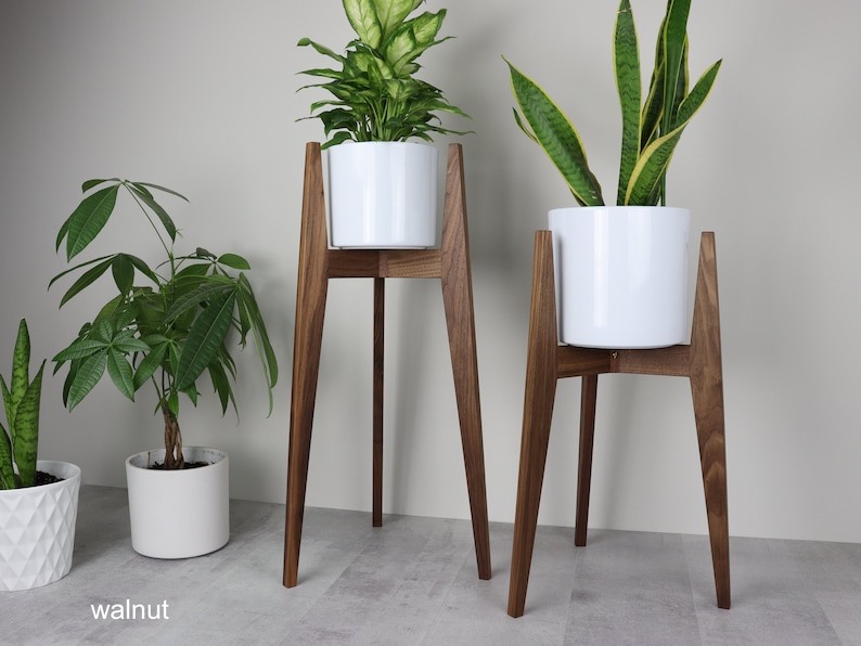 May include: Two white plant pots on wooden stands. The stands are made of walnut wood and have a mid-century modern design. The pots are both round and have a simple, modern design.