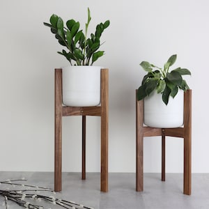 Puede incluir: Dos macetas de cer&aacute;mica blanca sobre soportes de madera. Los soportes son de madera de nogal y tienen un dise&ntilde;o simple y moderno. Las macetas est&aacute;n vac&iacute;as y listas para ser llenadas con plantas.