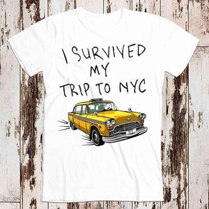 May include: White t-shirt with black text that reads "I survived my trip to NYC" and a yellow taxi cab illustration.