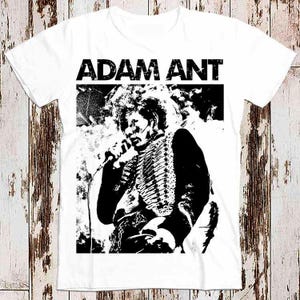 May include: White t-shirt featuring a black and white image of Adam Ant, a singer, holding a microphone. The text "ADAM ANT" is printed in black above the image.