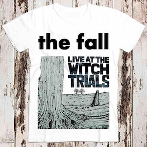 May include: White t-shirt featuring a black and white graphic print of a band called "the fall" with the text "Live at the Witch Trials".