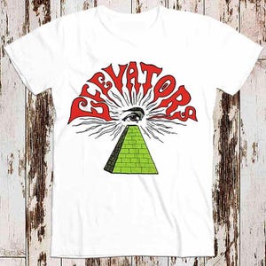 May include: White t-shirt featuring a red graphic of the word "Elevators" in a stylised font. The graphic depicts an eye within a pyramid with rays of light radiating from it.