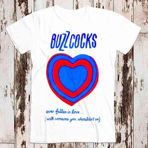 May include: White t-shirt with a red and blue heart graphic and the text "Buzzcocks" in blue. The text below the heart reads "ever fallen in love... (with someone you shouldn't've)"