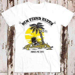 May include: White t-shirt featuring a black and yellow graphic of a palm tree on an island with a record player and the text "NEW FOUND GLORY" and "MAKES ME SICK".