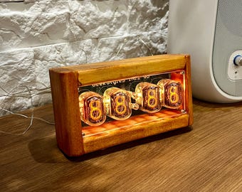 Könnte beinhalten: Eine Holzuhr mit vier leuchtenden orangefarbenen Nixie-Röhren, die die Zeit "88:88" anzeigen. Die Uhr ist mit "Dekatron IN12 6S" beschriftet und steht auf einer Holzoberfläche.