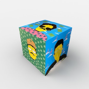 May include: A cube-shaped box with a colorful design featuring cartoon characters. The box has a green, blue, and pink background with images of people wearing hats and sunglasses. The box also has a pink flamingo and the word "money" printed on it.