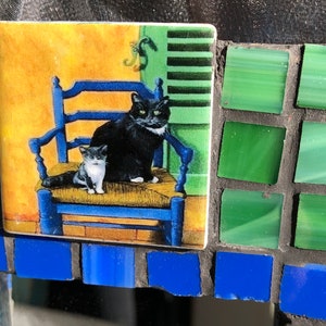 May include: A blue chair with a woven seat, a black cat and a smaller white and gray cat sitting on it. The chair is in front of a yellow wall with a green door and window.