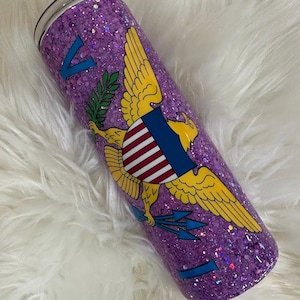 May include: A purple glitter tumbler featuring the Virgin Islands coat of arms. The design includes a yellow eagle with a shield, blue arrows, and the letter "V". The tumbler has a silver lid.