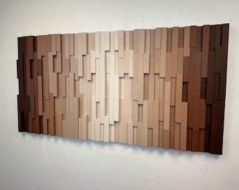 May include: A rectangular wall art piece composed of numerous vertical wooden slats of varying lengths and depths. The slats are arranged in a gradient color pattern, transitioning from dark brown on the outer edges to light cream in the center.