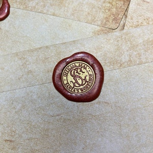 Op de afbeelding: Een close-up van een roodbruin waszegel met gouden letters met de tekst "OFFICIAL SEAL SANTA'S WORKSHOP". Het zegel bevindt zich op een cr&egrave;mekleurige envelop. De afbeelding is goed belicht en de details zijn duidelijk.