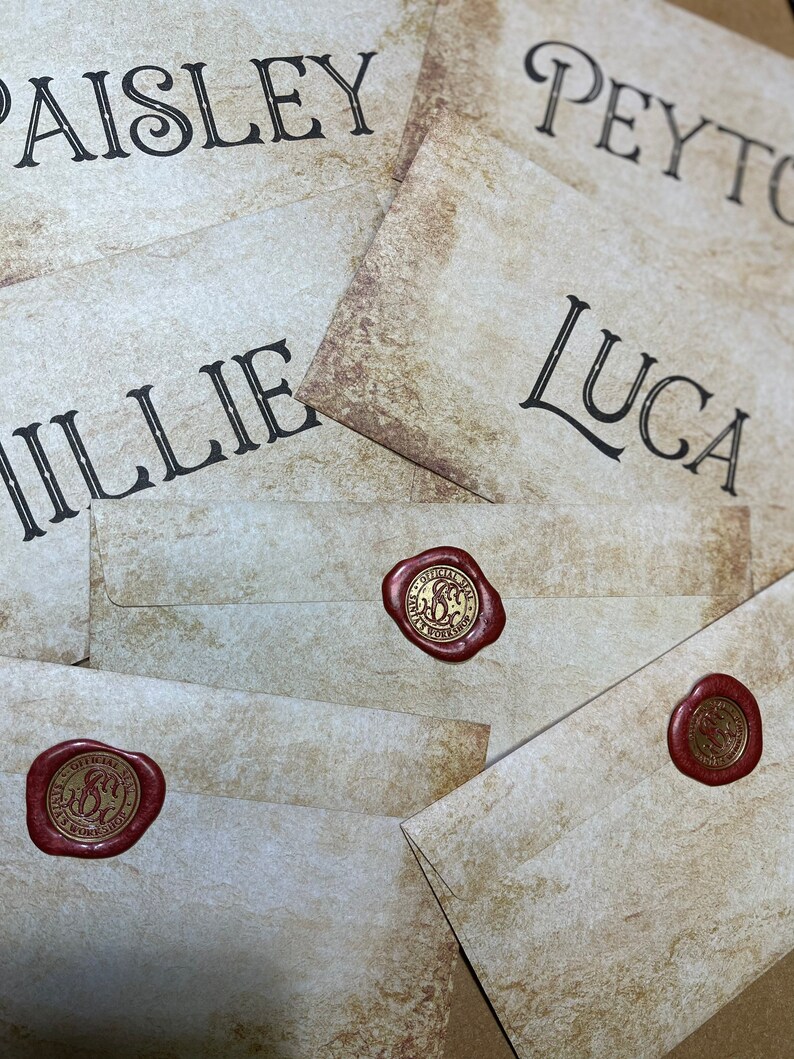Op de afbeelding: Close-up van verschillende cr&egrave;mekleurige enveloppen met namen in zwart script: Paisley, Peyton, Millie en Luca. Elke envelop is verzegeld met een rode waszegel. De zegels hebben een gouden embleem met de tekst "Official Seal, B's Workshop".