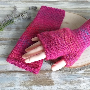 May include: Pink knitted fingerless gloves with a textured pattern. The gloves are made with a multi-colored yarn, including shades of pink, orange, and blue.