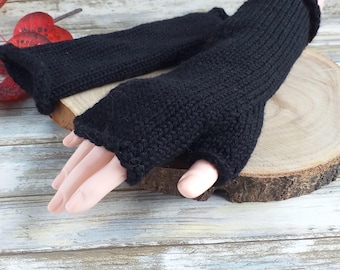 May include: A pair of black fingerless gloves featuring a ribbed knit texture. The gloves extend past the wrist and have a dedicated opening for the thumb, with a simple finished edge at the top and bottom openings of the garment.