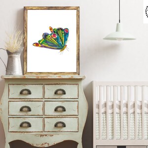 Op de afbeelding: Een kleurrijke vlinder met groene, blauwe, gele en rode vleugels is afgedrukt op een witte achtergrond. De print is ingelijst in een rustiek houten frame.