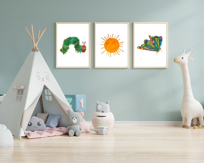 Op de afbeelding: Drie ingelijste prints op een lichtblauwe muur. De prints tonen een groene rups, een gele zon en een kleurrijke vlinder. Een witte tipi-tent met een grijze flap staat op de voorgrond.
