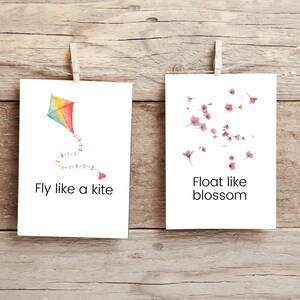 K&ouml;nnte beinhalten: Zwei wei&szlig;e Karten mit inspirierenden Botschaften. Die linke Karte zeigt einen bunten Drachen mit einem Herzen am Ende des Schwanzes und dem Text "Fly like a kite". Die rechte Karte zeigt rosa Kirschbl&uuml;ten und den Text "Float like blossom".