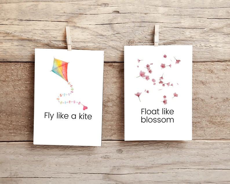 K&ouml;nnte beinhalten: Zwei wei&szlig;e Karten mit inspirierenden Botschaften. Die linke Karte zeigt einen bunten Drachen mit einem Herzen am Ende des Schwanzes und dem Text "Fly like a kite". Die rechte Karte zeigt rosa Kirschbl&uuml;ten und den Text "Float like blossom".