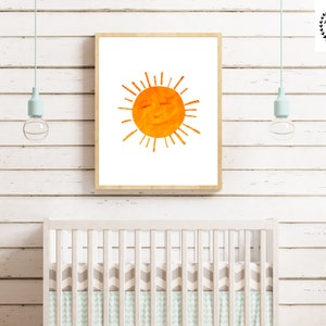 Op de afbeelding: Een ingelijst afdruk van een aquarel van een zon met een glimlachend gezicht. De zon is oranje en geel en de achtergrond is wit.