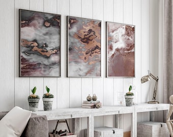 May include: Three abstract art prints with a white, gray, and pink background with gold accents. The prints are framed in a thin, silver frame and are hanging on a white wall.