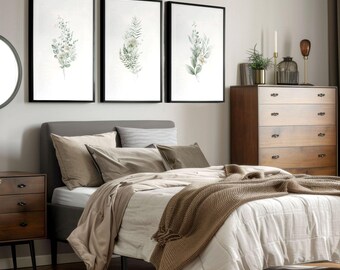 May include: Three framed watercolor prints of green botanical illustrations with white flowers on a white background. The prints are hanging on a light gray wall above a gray upholstered bed with brown bedding and a brown throw blanket.