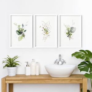 May include: Three framed wall art prints featuring watercolor illustrations of green eucalyptus leaves and berries. The artwork is displayed in white frames, showcasing botanical arrangements with soft green tones and gold-colored leaf outlines.