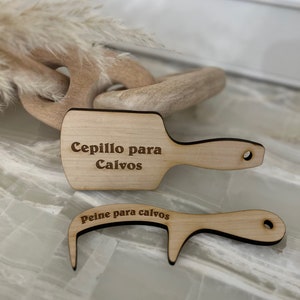 May include: Two wooden hair grooming tools. The top tool is a brush with the text "Cepillo para Calvos". The bottom tool is a comb with the text "Peine para calvos". Both tools are made of light-colored wood.