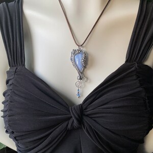May include: A silver wire wrapped pendant necklace with a blue agate stone. The necklace is on a brown leather cord.