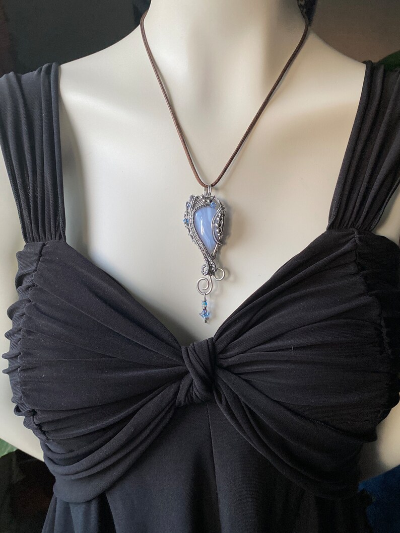 May include: A silver wire wrapped pendant necklace with a blue agate stone. The necklace is on a brown leather cord.