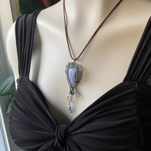 May include: A silver wire wrapped pendant necklace with a blue agate stone and a small star charm. The necklace is on a brown cord.