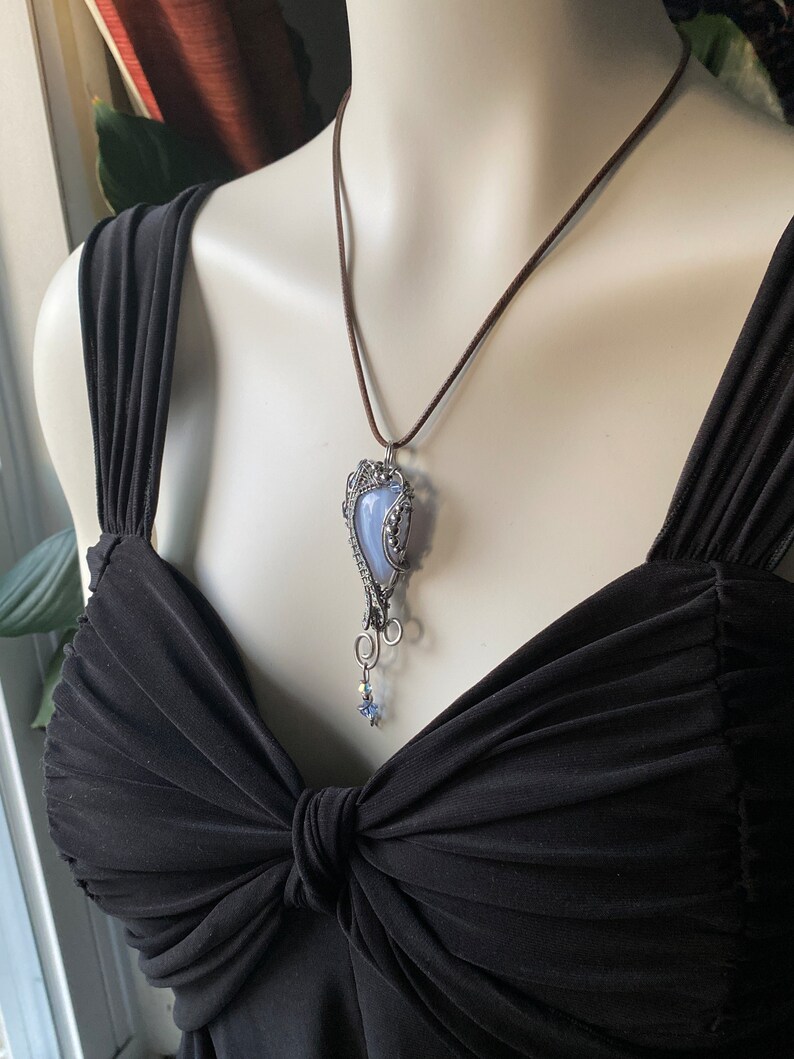 May include: A silver wire wrapped pendant necklace with a blue agate stone and a small star charm. The necklace is on a brown cord.