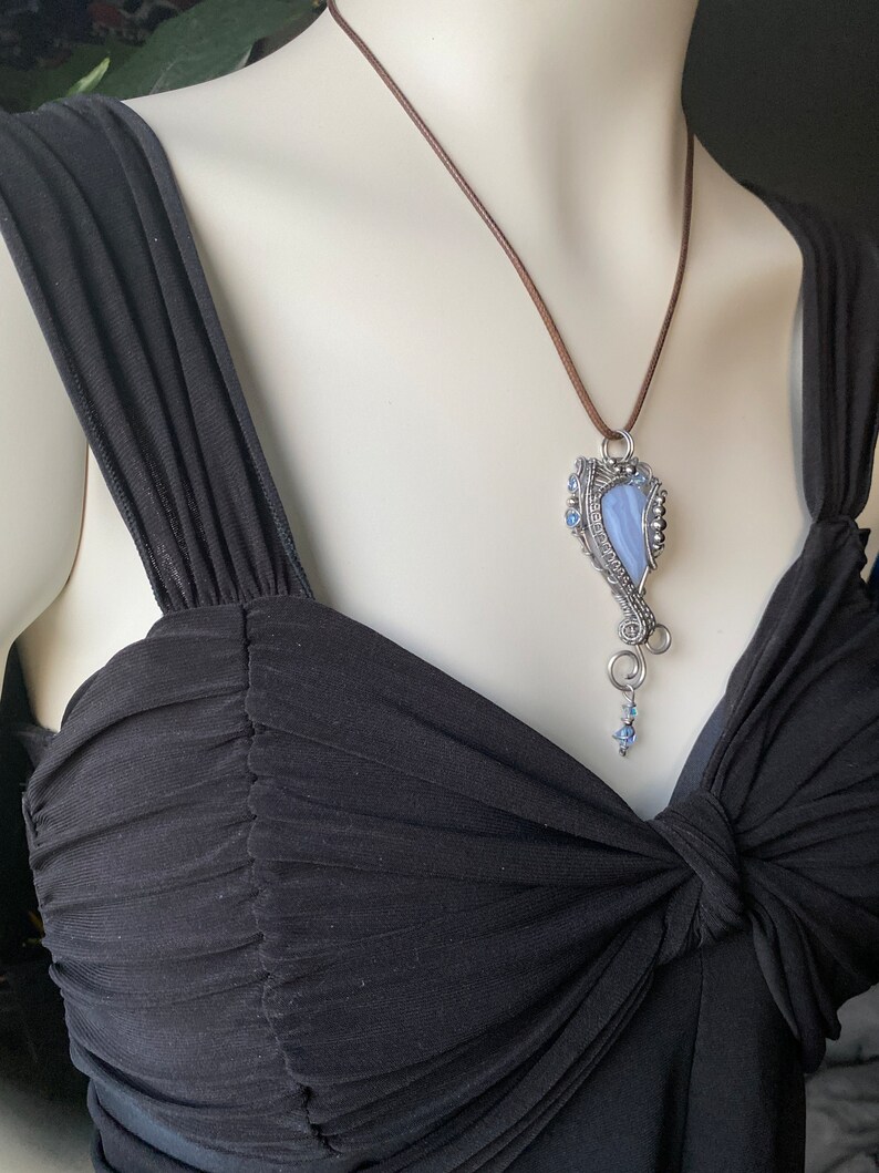 May include: A silver wire wrapped pendant featuring a blue agate stone with a brown leather cord necklace.