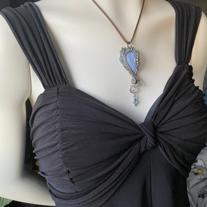 May include: A blue agate stone pendant with silver wire wrapping and blue crystal accents hangs from a brown leather cord.