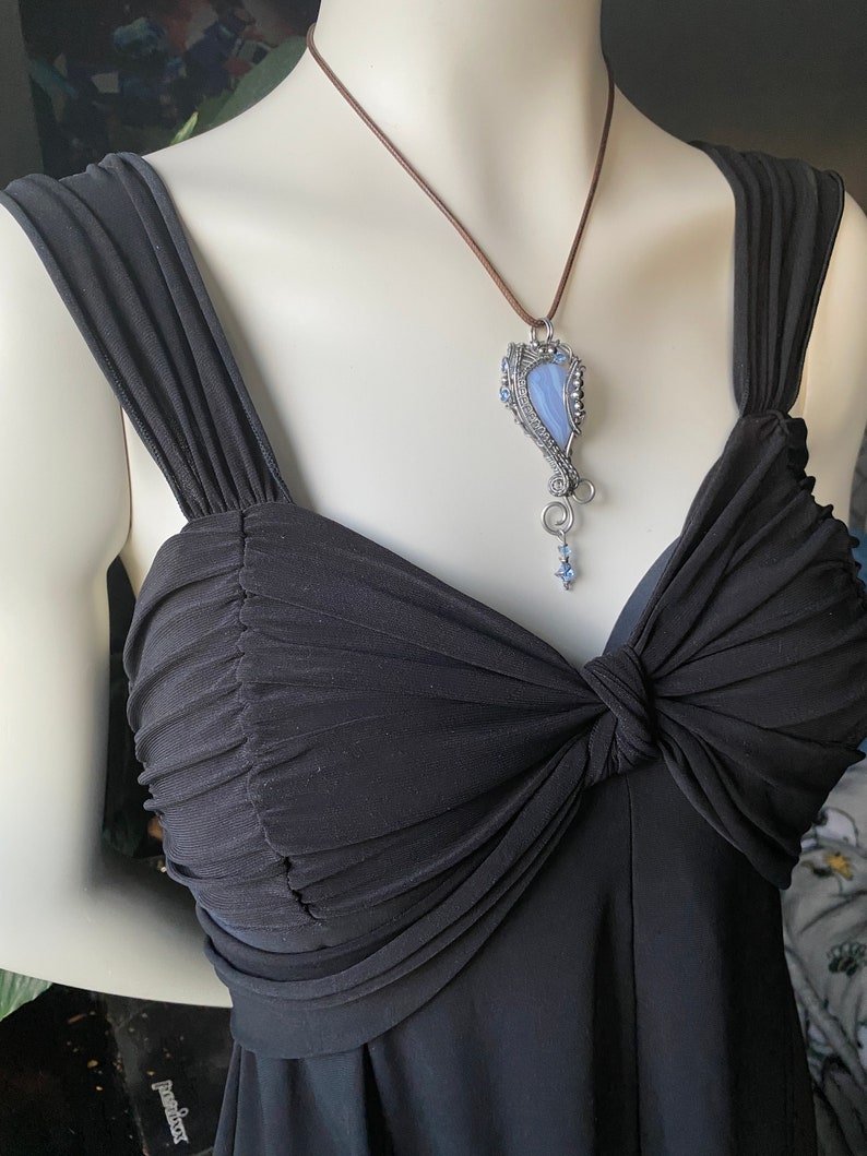 May include: A blue agate stone pendant with silver wire wrapping and blue crystal accents hangs from a brown leather cord.