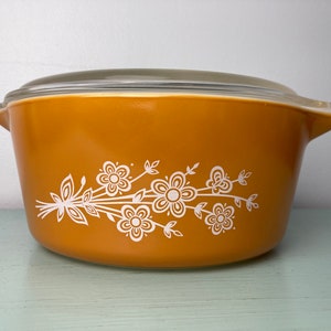 May include: A yellow casserole dish with a white floral design and a glass lid.