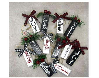 May include: A collection of 10 black and white wooden Christmas decorations with red and black buffalo check ribbon. The decorations are decorated with the words "Jingle", "Peace", "Joy", "Believe", "Merry", "Noel", "Jingle", "Peace", "Joy", and "Noel".