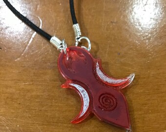 May include: A red and white pendant necklace with a unique design. The pendant is shaped like a teardrop with a spiral design in the center. The necklace is made of a black cord.