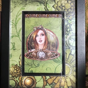 May include: A framed steampunk-style artwork featuring a woman with goggles and a clock face in a green and brown background with gears and other mechanical elements.