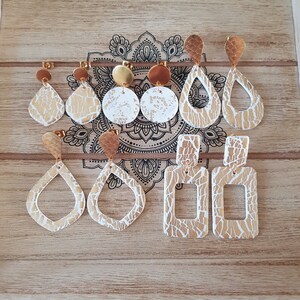 Puede incluir: Un conjunto de 9 pendientes de oro y blanco con diversas formas y diseños. Los pendientes se muestran sobre una superficie de madera.