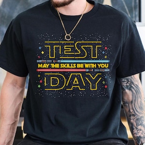 May include: Black t-shirt with a yellow and white graphic that says "TEST DAY" with a Star Wars theme. The graphic includes light sabers and the text "May the skills be with you".