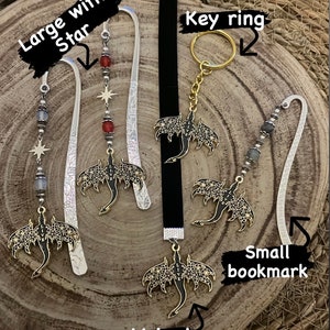 May include: A collection of fantasy-themed accessories, including bookmarks and a key ring. The bookmarks feature ornate metal dragon pendants with the word "LIVE" and decorative beads. One bookmark has a star charm. The key ring has a gold-colored ring.